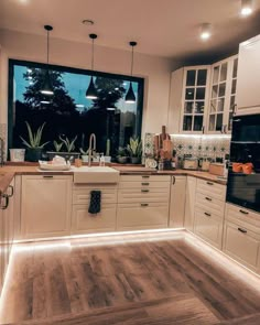 a kitchen with wooden floors and white cabinets, lights on the windows over the sink