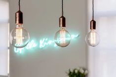 three light bulbs hanging from the ceiling in front of a wall with words on it