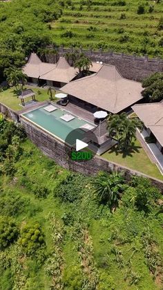 an aerial view of a house with a pool in the foreground and lush vegetation surrounding it