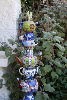 a stack of vases sitting on top of each other in front of some bushes