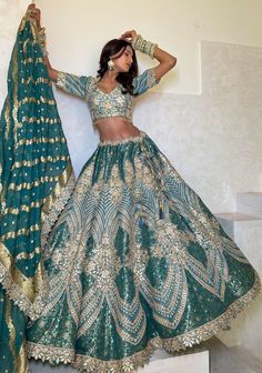 a woman in a green and gold lehenga with her hands on her head