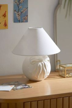 a white lamp sitting on top of a wooden table next to a mirror and pictures