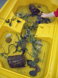 a child playing in a yellow plastic boat filled with rocks, plants and other things