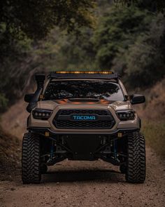 the front end of a truck driving down a dirt road with trees in the background