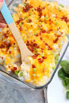 a person holding a wooden spoon over a casserole dish with cheese and bacon