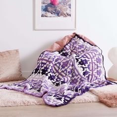 a purple and white blanket sitting on top of a wooden floor next to two pillows