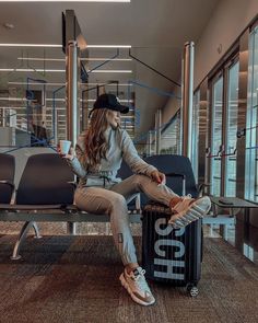 a woman sitting on top of a luggage bag next to an empty chair in an airport