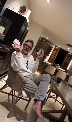 a man sitting at a table with cards in front of him, holding up two playing cards