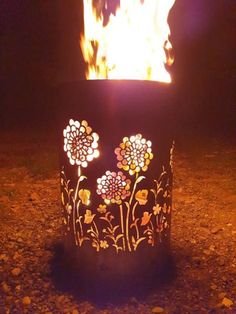 a fire pit with flowers painted on it in the dark, surrounded by rocks and gravel