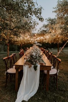 an outdoor dinner table set up with flowers and greenery on the table, surrounded by string lights