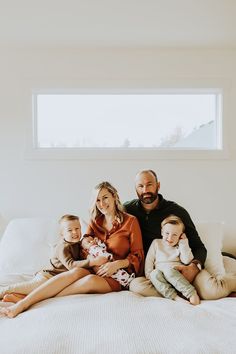 a family sitting on a bed with their baby's hands in their pockets and smiling at the camera