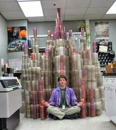 a man sitting on the floor in front of a pile of toilet paper rolls that are stacked high