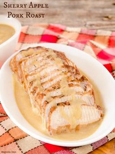 a white plate topped with meat covered in gravy next to a bowl of soup