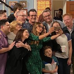 a group of people standing around each other in front of a staircase with one woman taking a selfie