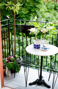 a small table with two cups on it next to a potted plant and some flowers