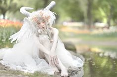 a woman dressed in white sitting next to a body of water with horns on her head