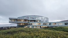 an unusual building sits on the edge of a grassy hill near the ocean and water