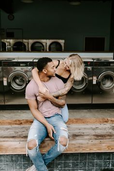 a man and woman sitting on top of each other in front of washer machines