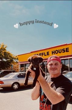 a man holding up a dog in front of a happy instead store with cars parked behind him