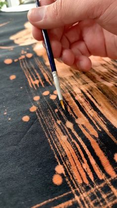 a person is holding a pen and writing on a piece of fabric with orange spots