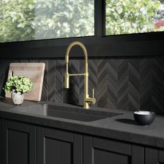 a kitchen with black cabinets and a gold faucet next to a sink in front of a window