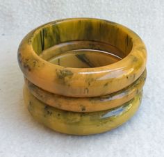 "A Splendid 1940's Assembled Set Of 3 Stacking End Of Day Ink Spot Bakelite Bangle Bracelets In Excellent Vintage Condition.  These 3 Bakelite bangle bracelets complement each other very nicely. The colors are butterscotch, caramel, blue moon, green, and black. The Mid Century Modern Bakelite bangles have marvelous patina to them. The 2 thick and chunky bracelets each measure 11/16\" wide with the outside diameter measuring 3 1/4\" and the inside 2 1/2\".  The center tube spacer bangle measures 3/8\" wide, outside diameter is 3 1/4\" and the inside diameter is 2 1/2\". All of bangles are free of any damage.  Imagine the envy of your friends who collect Bakelite when they see you with these 3 matching end of day ink-spot Bakelite Bangles in excellent vintage condition.  They tests positive Vintage Yellow Round Bracelets, Vintage Bakelite Bangle Jewelry, Vintage Bakelite Bangle, Vintage Bakelite Bracelet, Handmade Vintage Yellow Bracelets, Butterscotch Caramel, Bakelite Bracelets, Bakelite Bangles, End Of Days