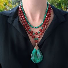 a woman wearing a green and red beaded necklace with a large tear shaped pendant