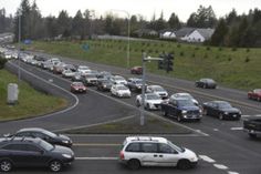 many cars are driving down the road in traffic on a cloudy day with green grass and trees behind them