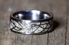 a wedding band with white flowers and leaves inlayed to it on a wooden surface