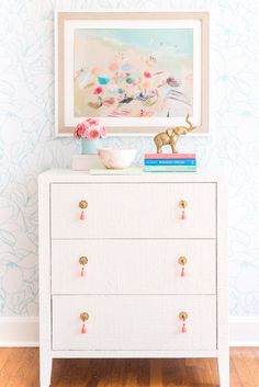 a white dresser with pink flowers on the top and blue wallpaper in the background