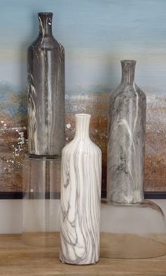 three vases sitting on top of a wooden table next to a wall with a painting in the background