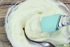 whipped cream in a glass bowl with a blue mixer attachment on the side and a wooden spoon