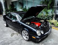 a black car with its hood open parked in front of a glass windowed building