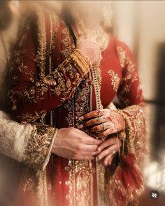 a woman in a red and gold wedding outfit holding her hands together while she is dressed up