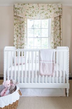 a white crib in front of a window with pink curtains