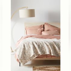 a bed with pink sheets and pillows in a white room next to a floor lamp