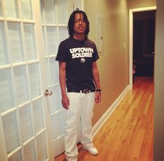 a young man standing in front of a door wearing white pants and a black shirt