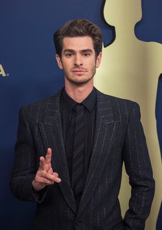 a man in a suit and tie standing next to an oscars red carpet with his hand up