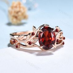 a close up of a ring with a red stone in the center and leaves around it