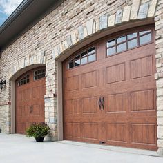 two brown garage doors are open in front of a brick wall and planter on the sidewalk