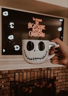 someone holding up a coffee cup with a skeleton face on it in front of a fireplace