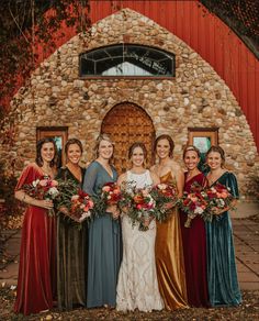 a group of women standing next to each other in front of a stone building holding bouquets