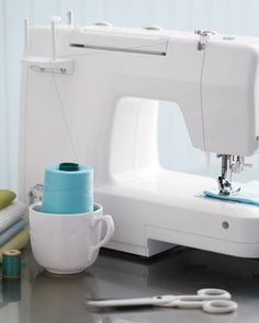 a white sewing machine sitting on top of a table next to a cup and scissors