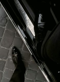 a black and white photo of someone's feet on the ground next to a car