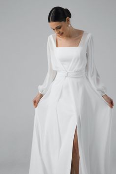 a woman is wearing a white dress with long sleeves and a slited skirt, while she