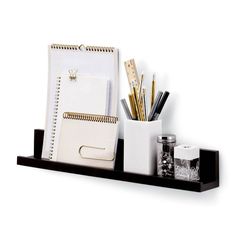 a black shelf with notebooks, pens and pencils on it next to other office supplies