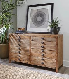 a wooden dresser with metal knobs and drawers in a living room next to a potted plant