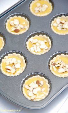 an uncooked muffin tin filled with mini pies covered in almonds