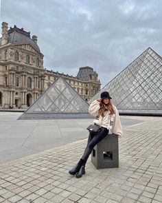 a woman sitting on top of a cement block next to a building with pyramids in the background