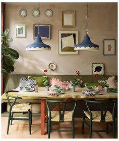 a dining room table with green chairs and pictures on the wall above it, along with hanging lights